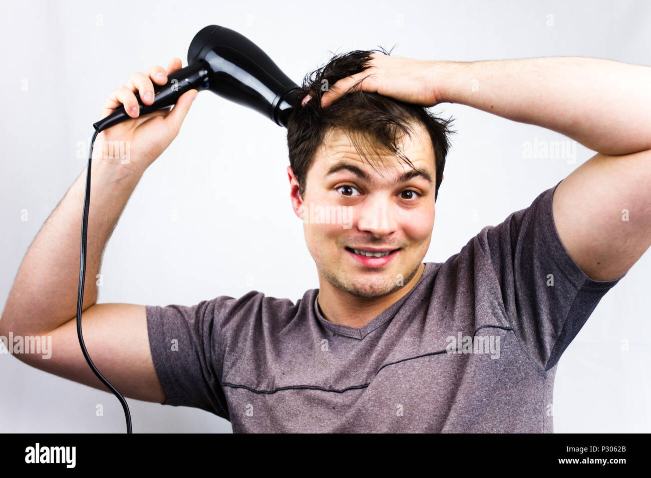 Joven sonriente mientras se seca el pelo. Adolescente sujetando el pelo  ventilador eléctrico. Joven seca el cabello con un ventilador eléctrico.  Preparando un pelo para ir t Fotografía de stock - Alamy