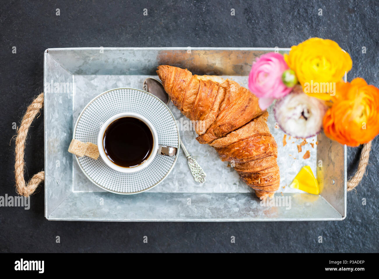 Desayuno ligero desde croissants frescos y una taza de café en la bandeja gris, Ranunculus flores cerca Foto de stock