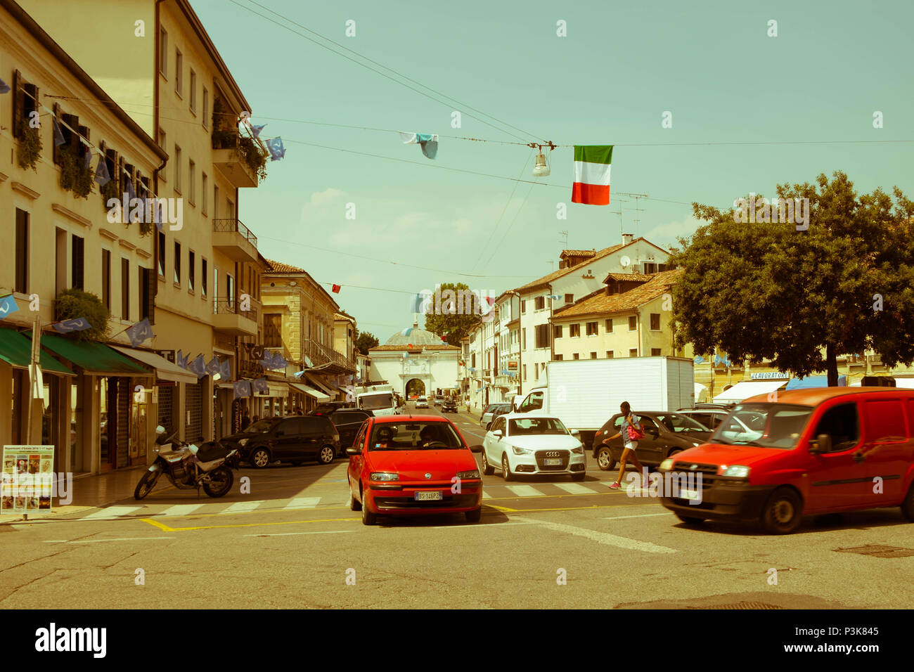 Un coche espera a otro coche para pasar a una intersección. Un peatón camina sobre el paso de cebra. Esta es la vida cotidiana en la ciudad de Treviso. Foto de stock