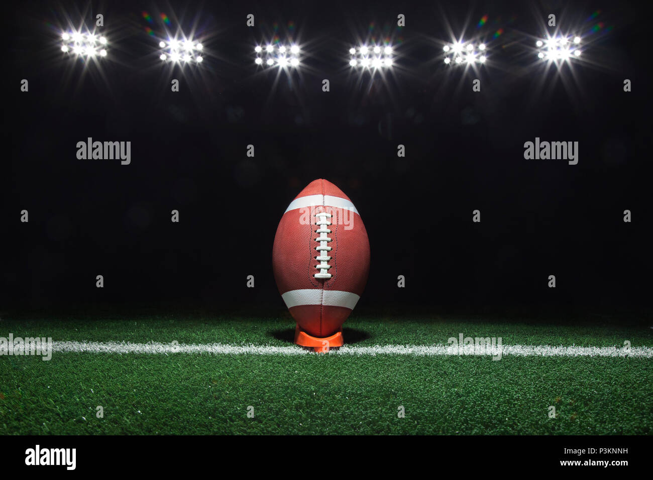 Una pelota de fútbol en una t en una yarda línea bajo luces de noche Foto de stock