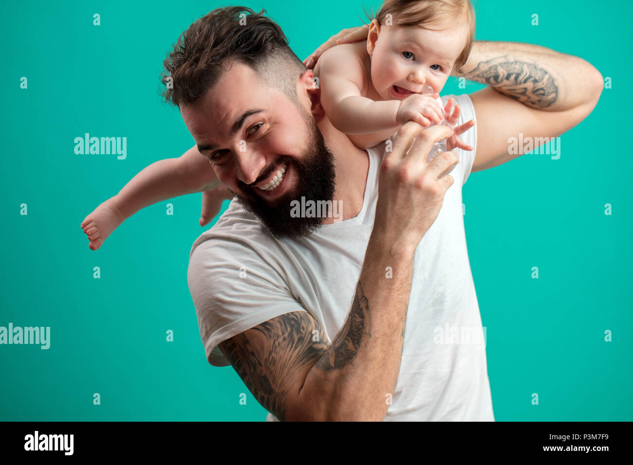 Juguetón padre llevar a su niño sonriente en cuello sobre fondo azul. Foto de stock