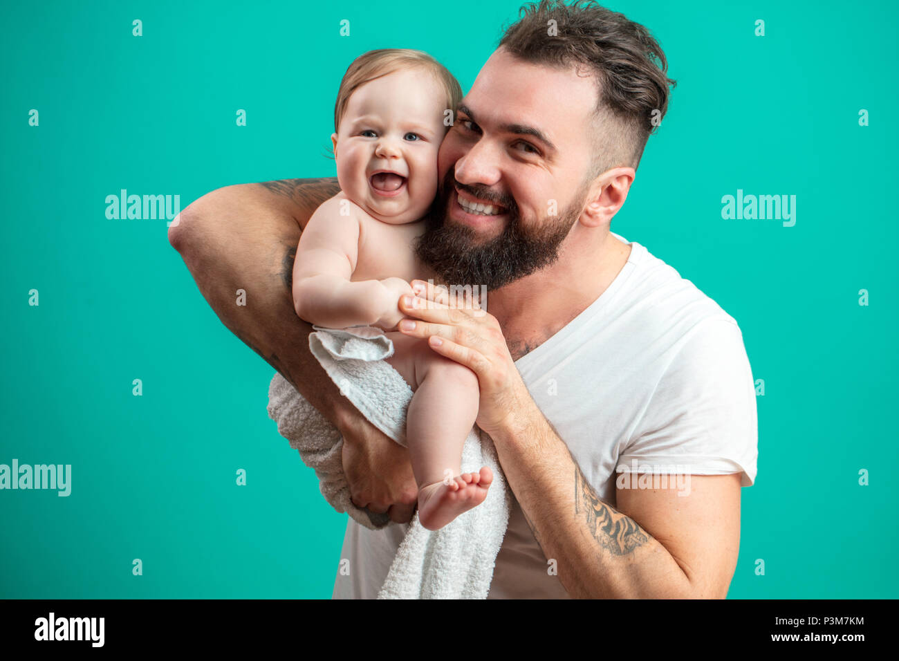 Juguetón padre llevar a su niño sonriente en cuello sobre fondo azul. Foto de stock