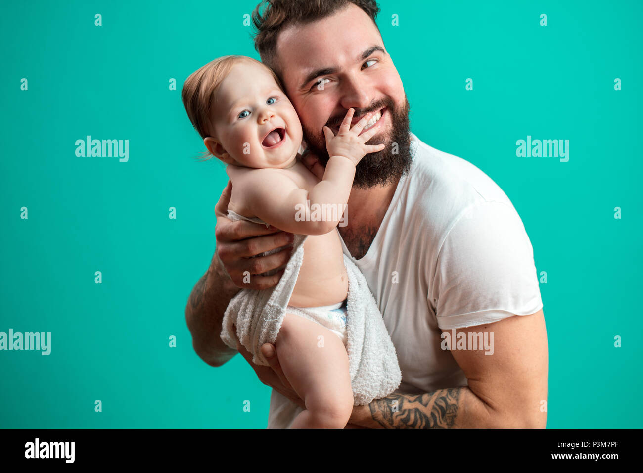 Juguetón padre llevar a su niño sonriente en cuello sobre fondo azul. Foto de stock