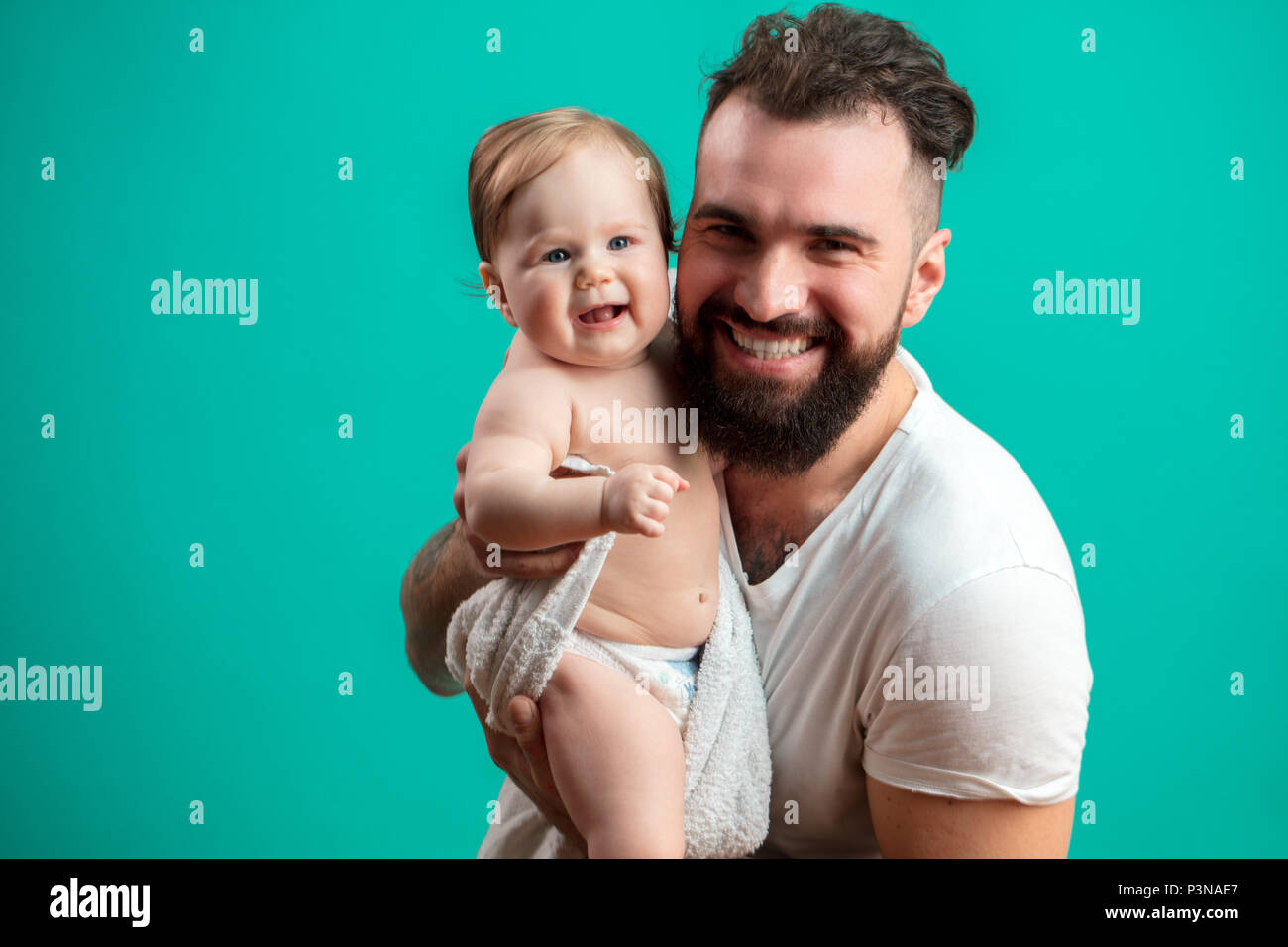 Juguetón padre llevar a su niño sonriente en cuello sobre fondo azul. Foto de stock