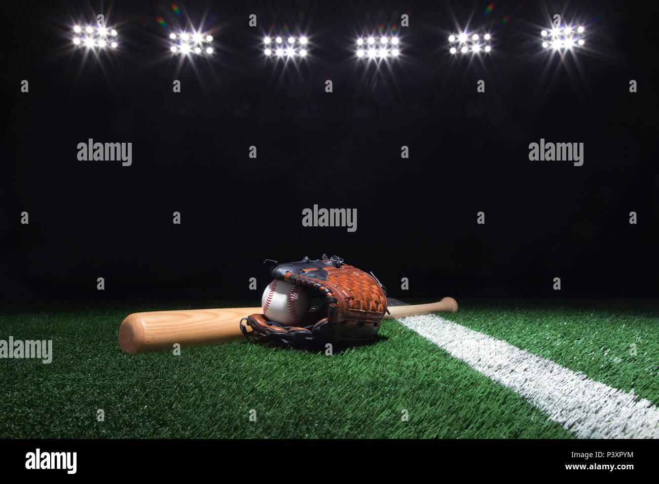 Béisbol, mitt y bat en campo de hierba con raya bajo las luces por la noche Foto de stock