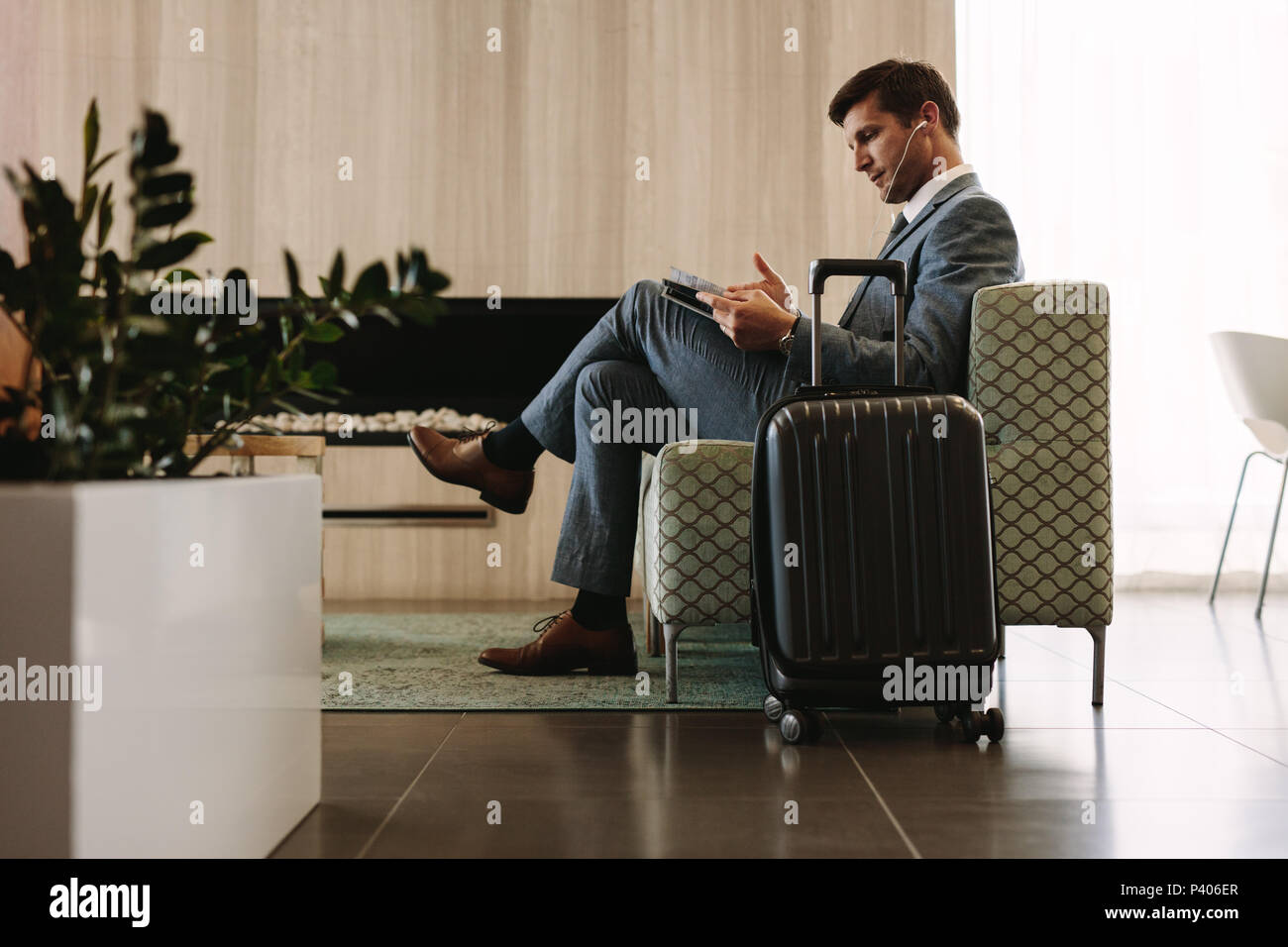 Empresario leyendo una revista mientras espera su vuelo en la terminal aérea lounge. Empresario en el área de espera del aeropuerto leyendo una revista. Foto de stock