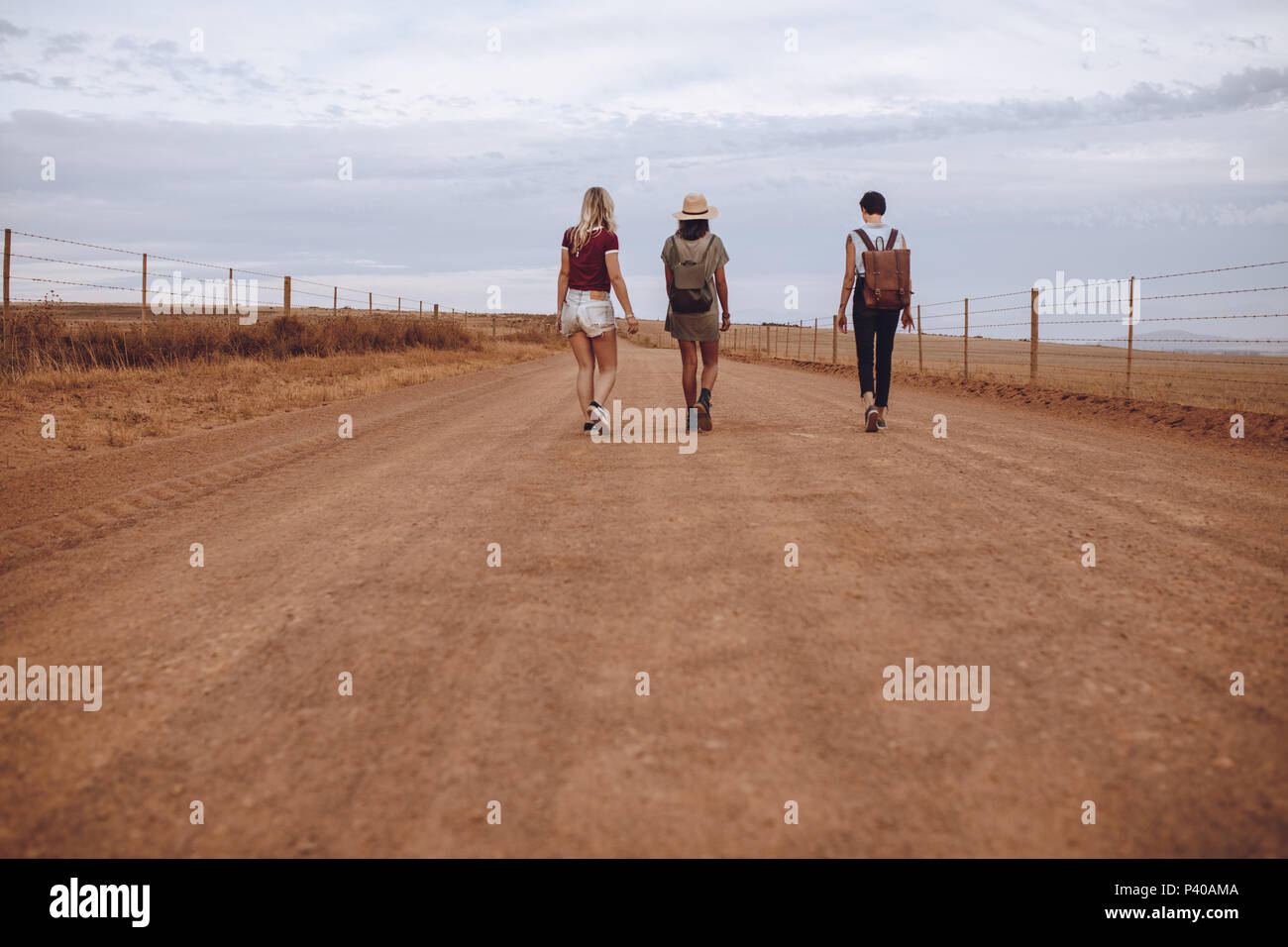 Vista trasera de tres jóvenes mujeres caminando por la carretera rural. Amigas caminando por una carretera rural. Foto de stock