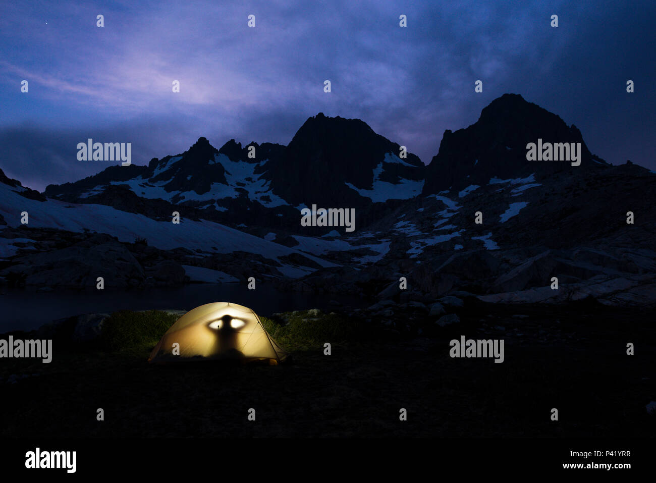 Camping y persona dentro de glowing carpa al anochecer con el banner y Ritter picos en el fondo en el desierto Ansel Adams de la Sierra, California. Foto de stock