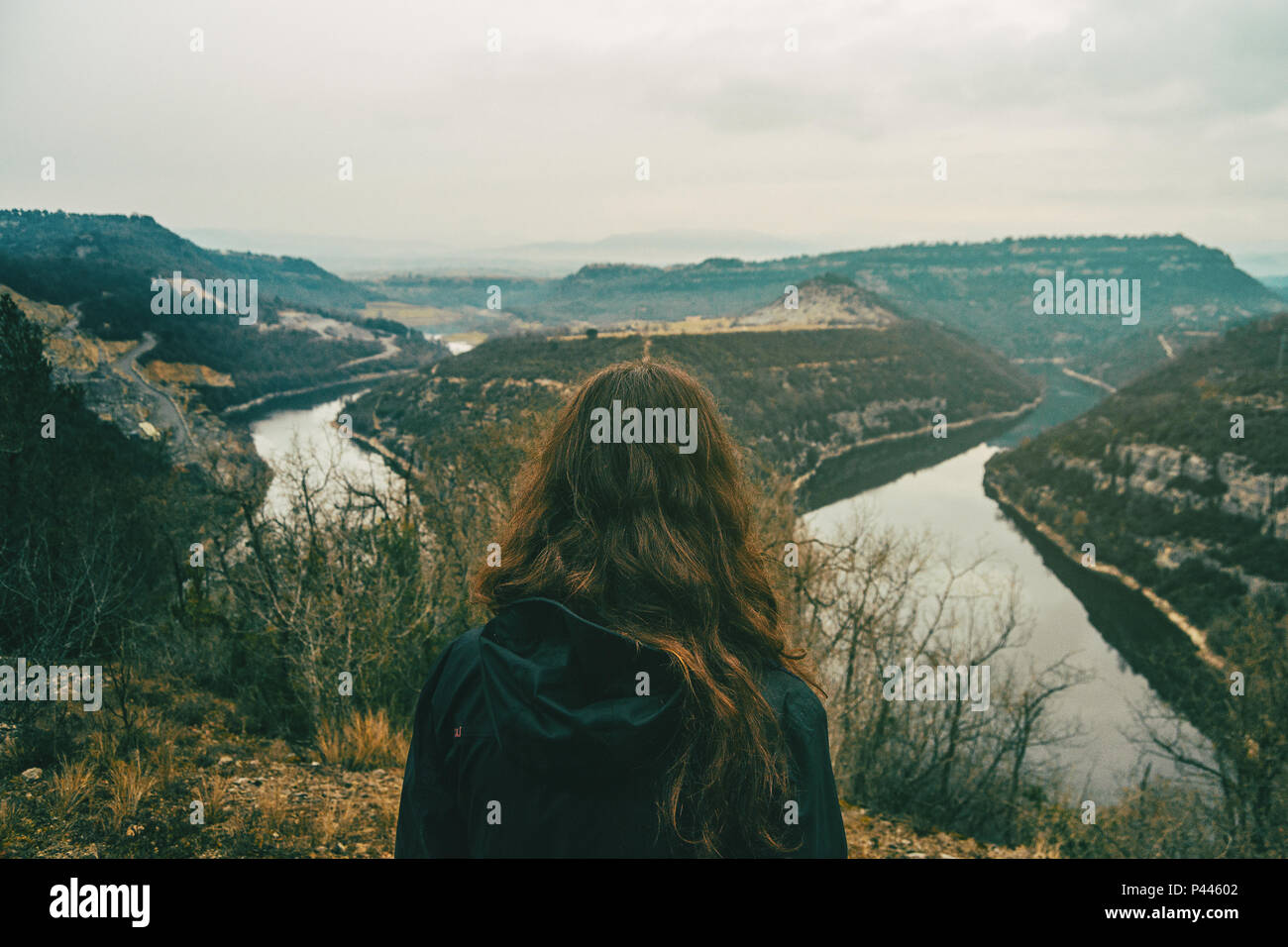 Chica desde atrás mirando los dos caminos del meandro de un río en un día nublado Foto de stock