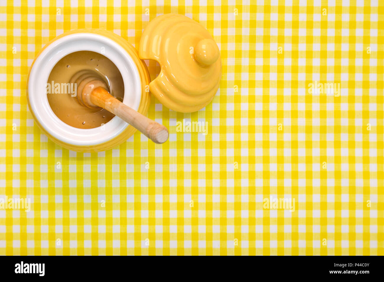 Una colmena themed olla llena de miel Manuka con penetrador de madera sobre un fondo amarillo - Cuadros con espacio de copia. Foto de stock