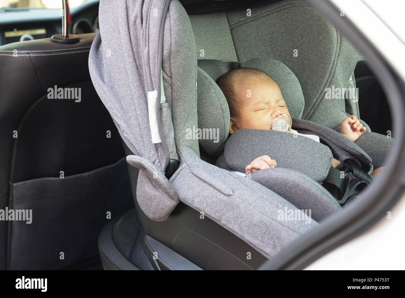 Asia un mes lindo bebé recién nacido duerme en el asiento de coche moderno.  Niño recién nacido, viajar, seguridad en la carretera. Una manera segura de  viajar abrochados los cinturones de seguridad