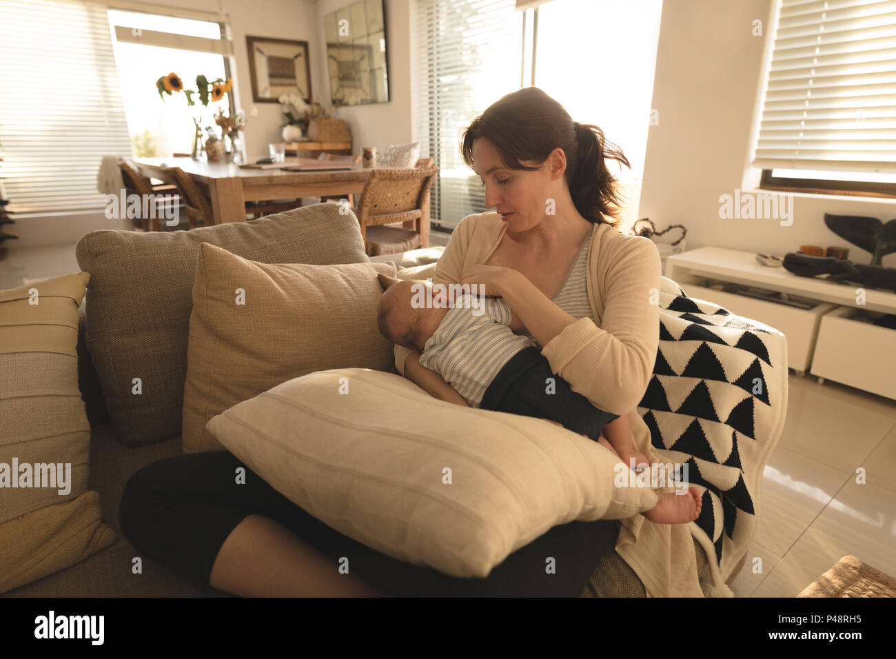 Mamá joven sentado en un sofá de amamantar a su bebé en la sala de estar  Fotografía de stock - Alamy