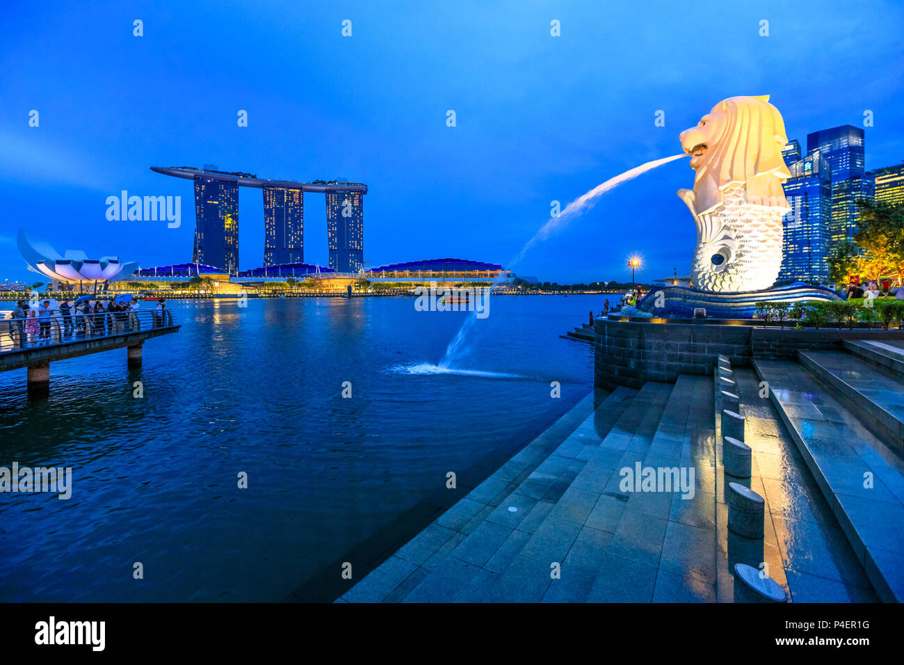 Singapur - Abril 27, 2018: reflexión estatua Merlion de Singapur en Marina Bay el mar. Merlion tiene una cabeza de león y cuerpo de pez y chorreando agua de su boca. Marina Bay Sands torres en el horizonte. Foto de stock