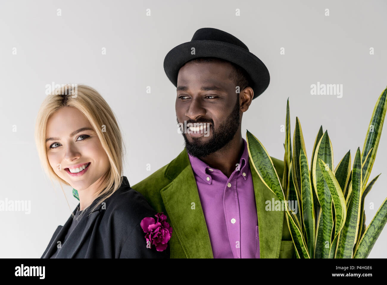 Retrato de sonriente pareja interracial elegante con el verde de las plantas en maceta aislado en gris Foto de stock