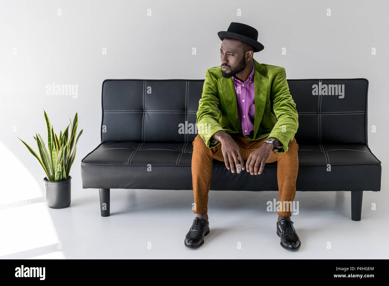 Pensativo moda hombre afroamericano en hat sentado en un sofá negro Foto de stock