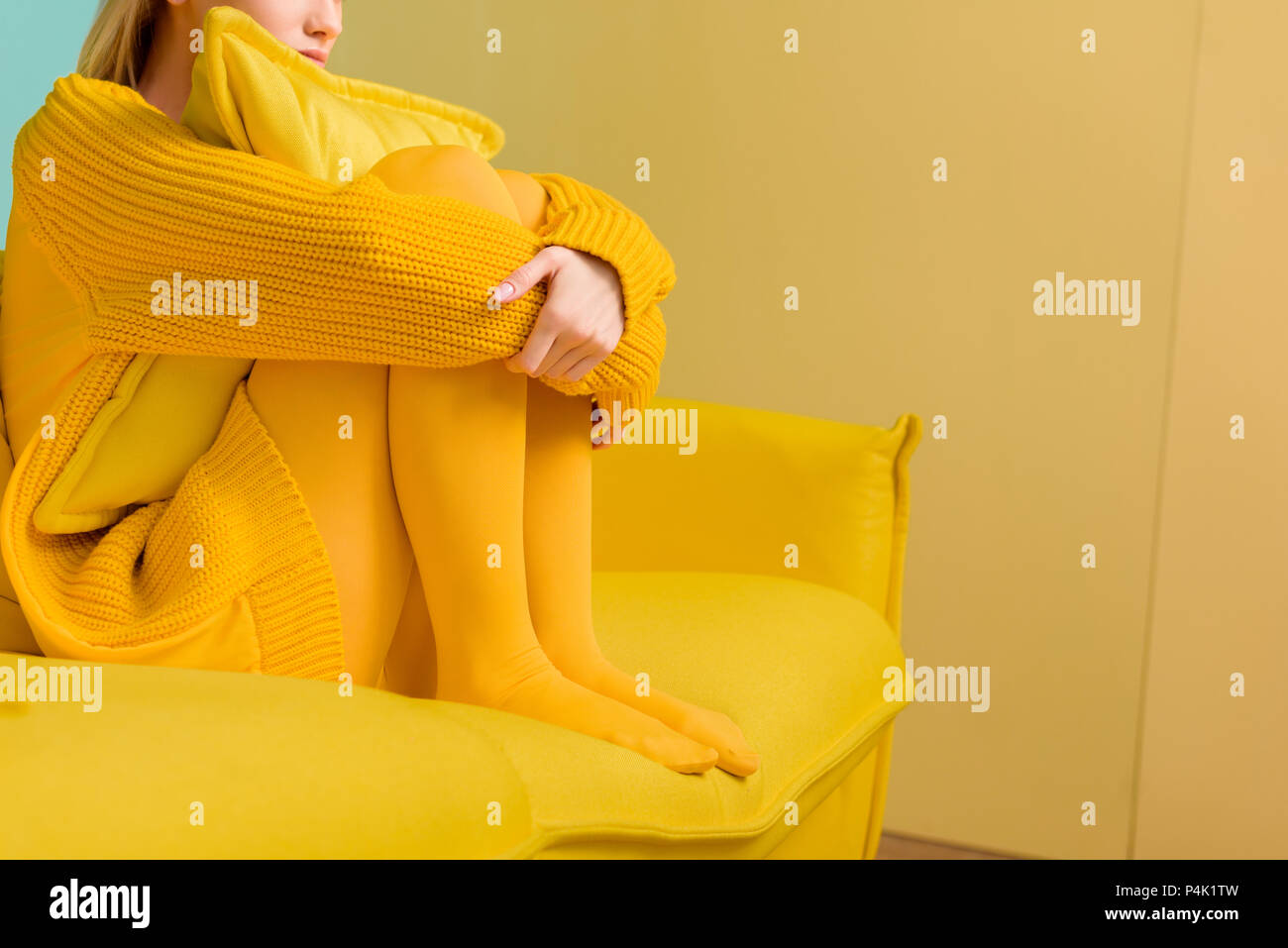 Vista parcial de la mujer en jersey amarillo y leotardos sentado en el sofá  amarillo Fotografía de stock - Alamy