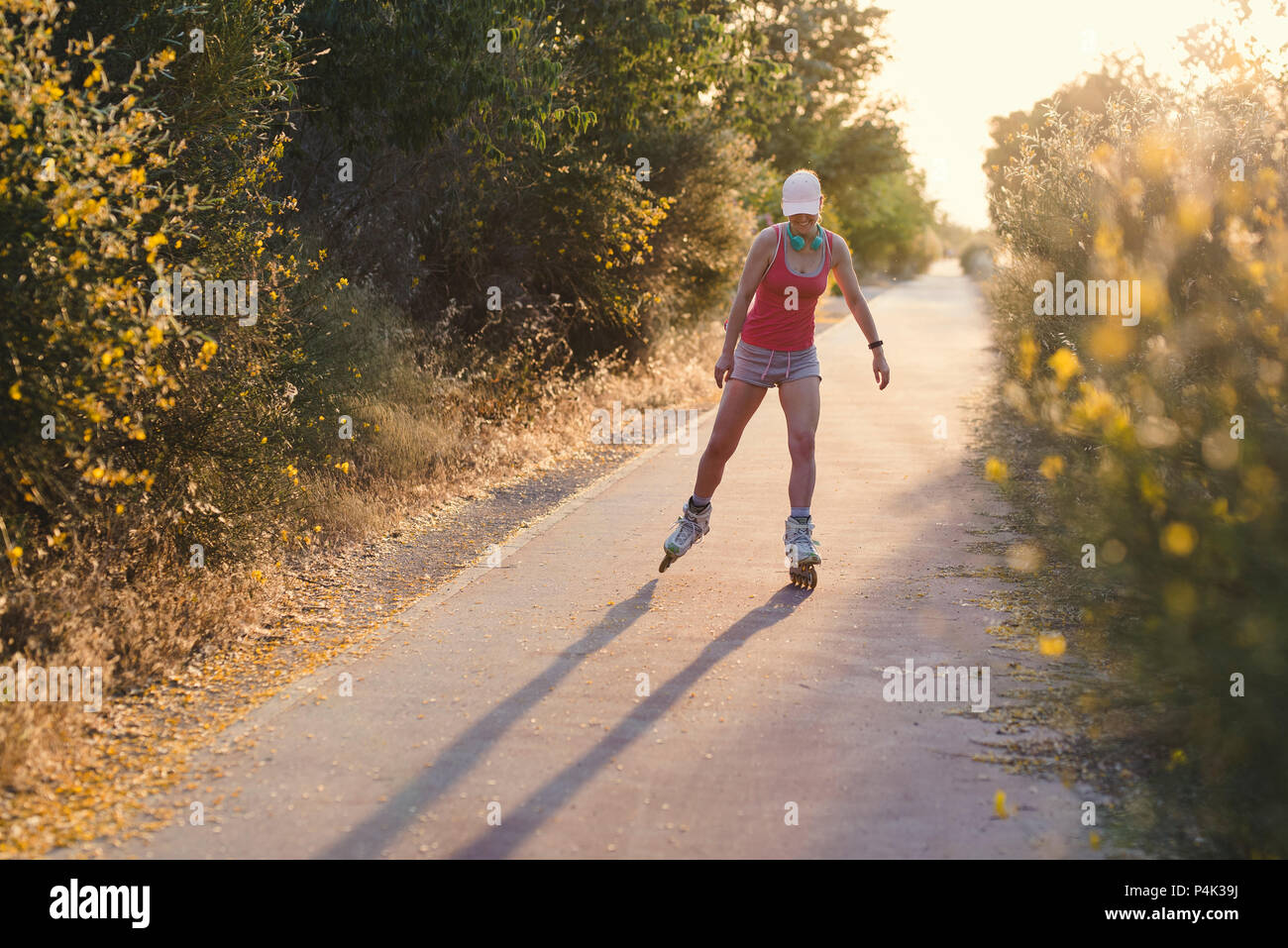 Mujer joven divirtiéndose mientras patinar al aire libre durante la puesta de sol. Atractivo femenino llevaba una tapa de color rosa pálido y ropa deportiva haciendo ejercicio mientras Foto de stock