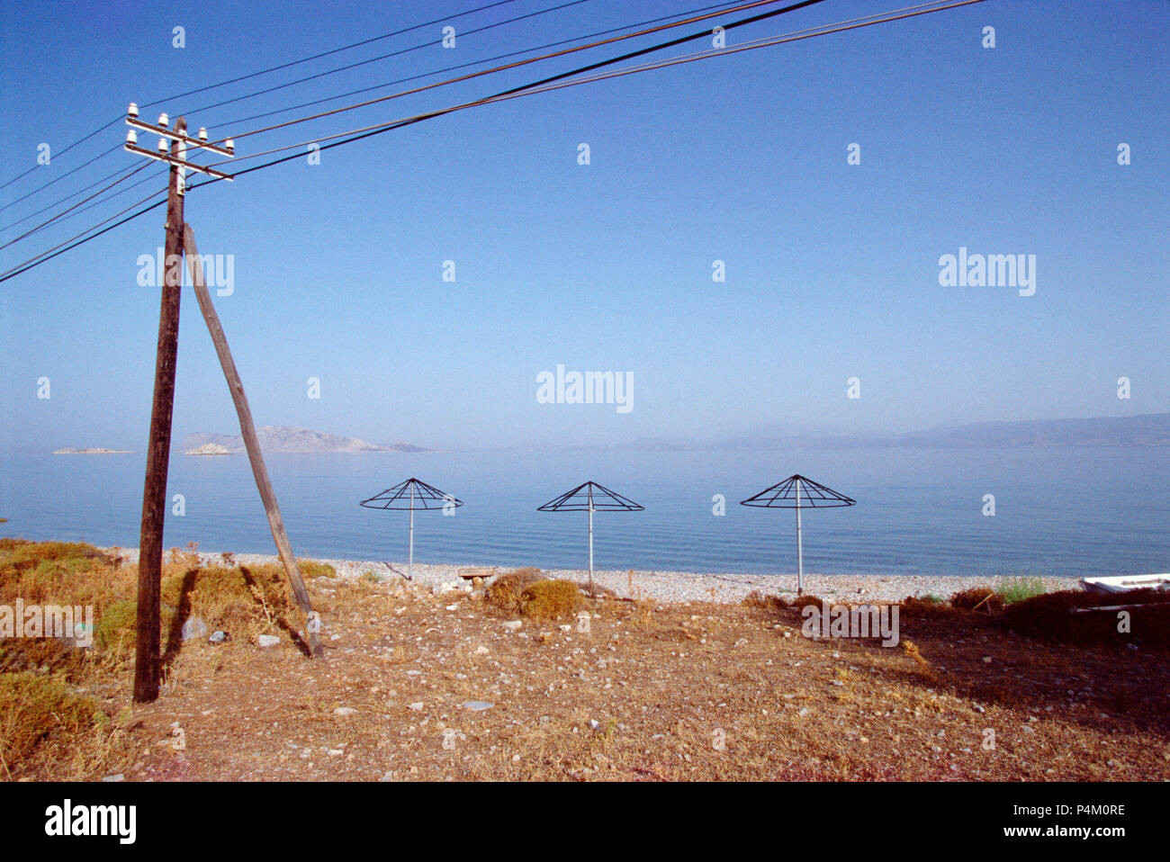 Vacía la playa de grava en la isla de Hydra, Grecia. No es muy atractivo, con los cables de alimentación y las disfunciones de la sombrilla Foto de stock