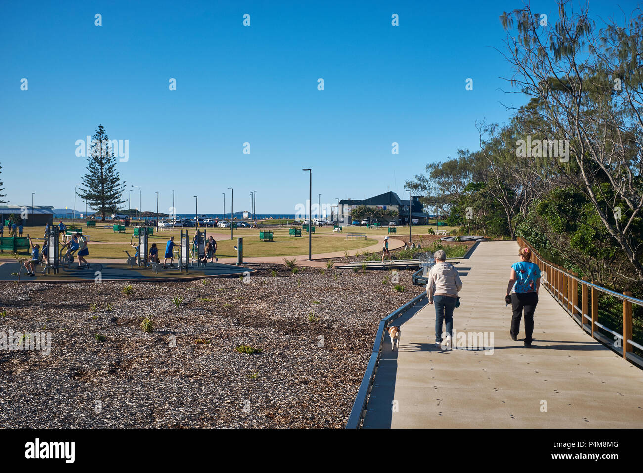 Dos personas caminando por una acera en el Jetty costas Park en un brillante cielo despejado, embarcadero, Playa, en Coffs Harbour, en Nueva Gales del Sur, Australia Foto de stock