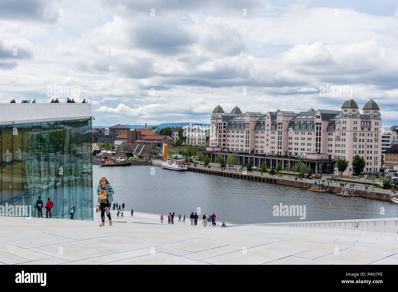Los turistas que caminan por el lado de la Ópera de Oslo, con la construcción de vidrio, personas con vistas a la terraza y grandes almacenes en segundo plano. Foto de stock