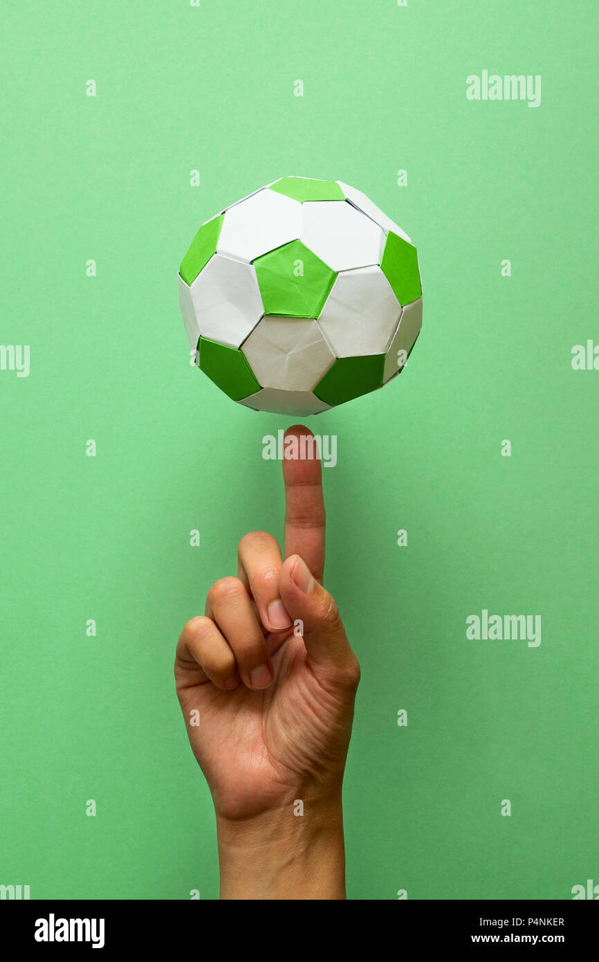 Mano girando el papel pelota de fútbol sobre fondo verde. El origami. Papel  Artesanal. Concepto de juego de fútbol Fotografía de stock - Alamy