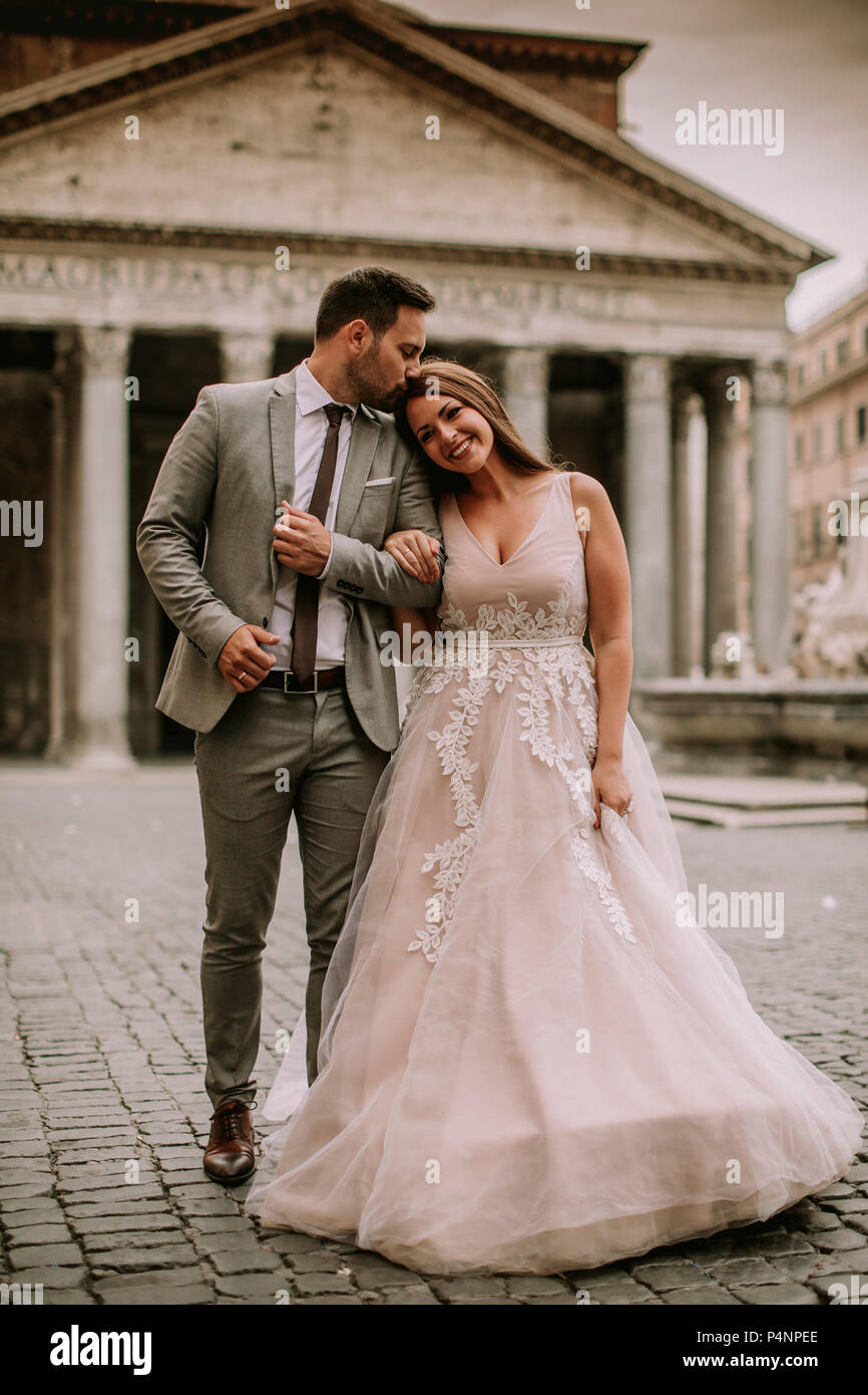 Atractivas jóvenes recién casados caminando y posando en Roma con hermosa y antigua arquitectura en el fondo en el día de su boda Foto de stock