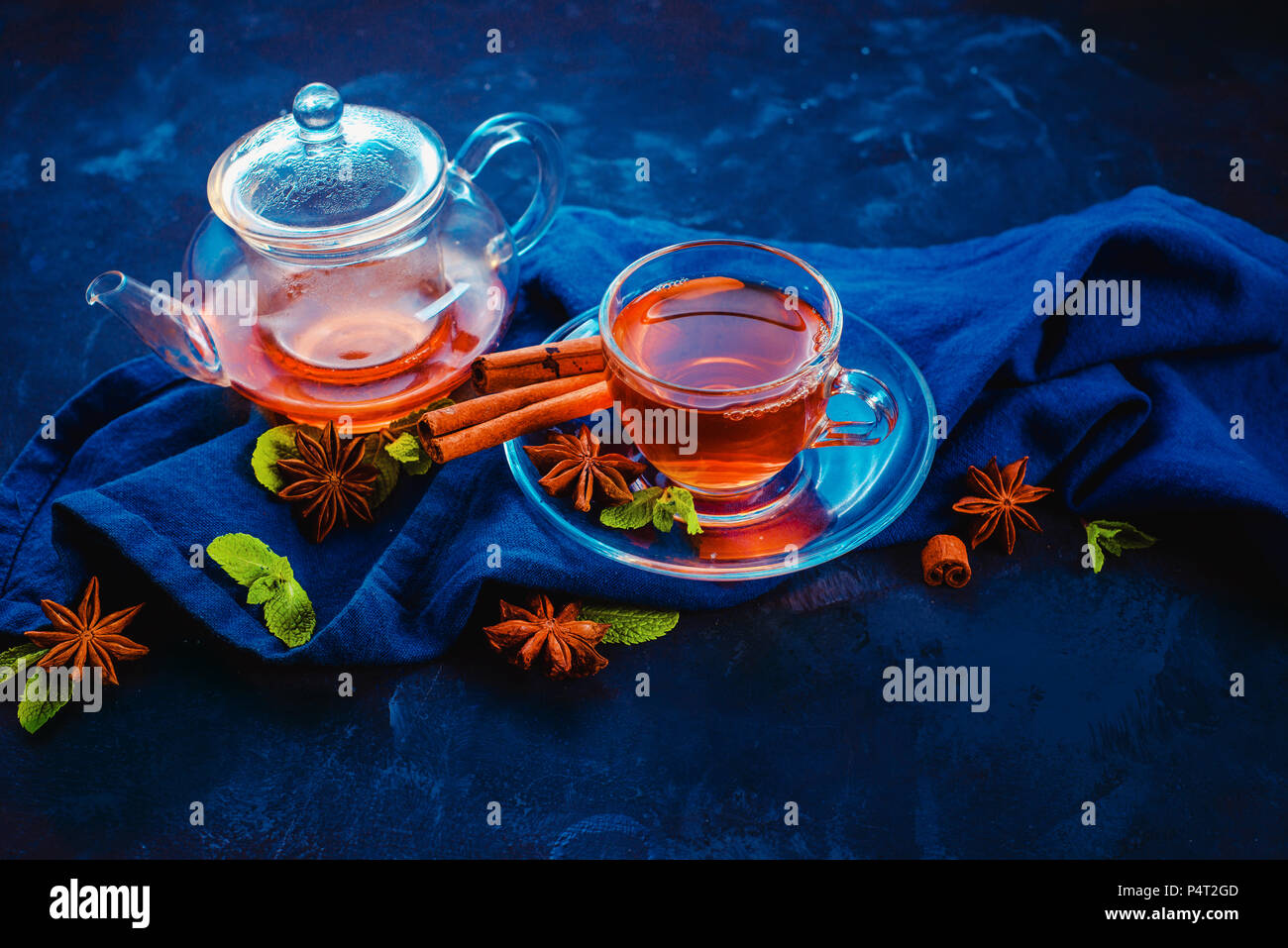 Té negro en un vaso y una pequeña tetera con rodajas de limón y hojas de menta sobre un fondo oscuro. Colores vibrantes bebida caliente cabezal con espacio de copia. Foto de stock