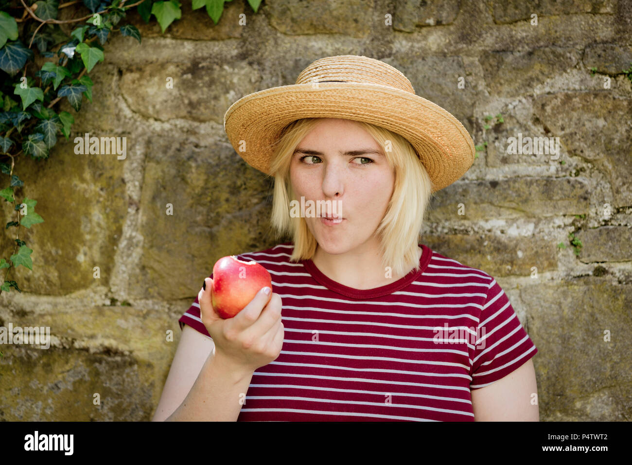 Retrato de joven mujer rubia con sombrero para el sol comiendo apple Foto de stock