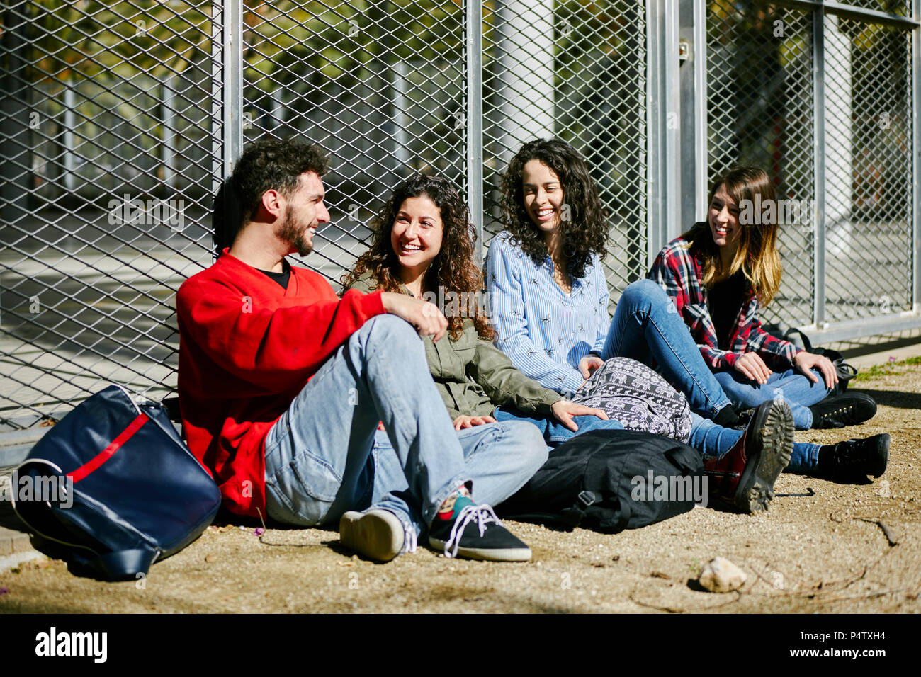 Cuatro amigos feliz sentado en la valla hablando Fotografía de stock - Alamy