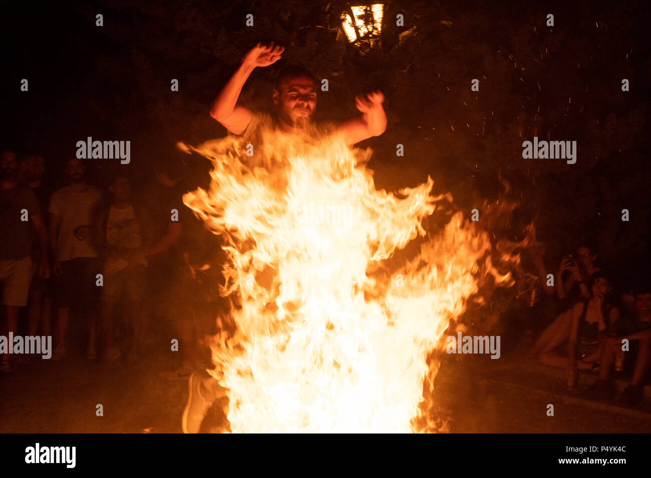 Madrid, España. 23 de junio de 2018. Un hombre saltando a través del fuego  de una fogata durante la víspera de San Juan en Madrid rodeado por cientos  de personas. © Valentin