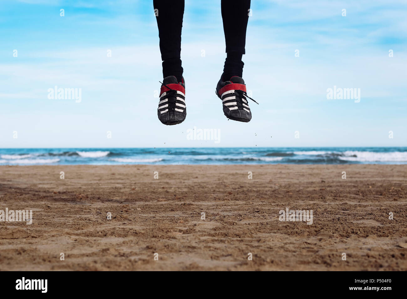 Las piernas del hombre saltando en el aire en la playa Foto de stock