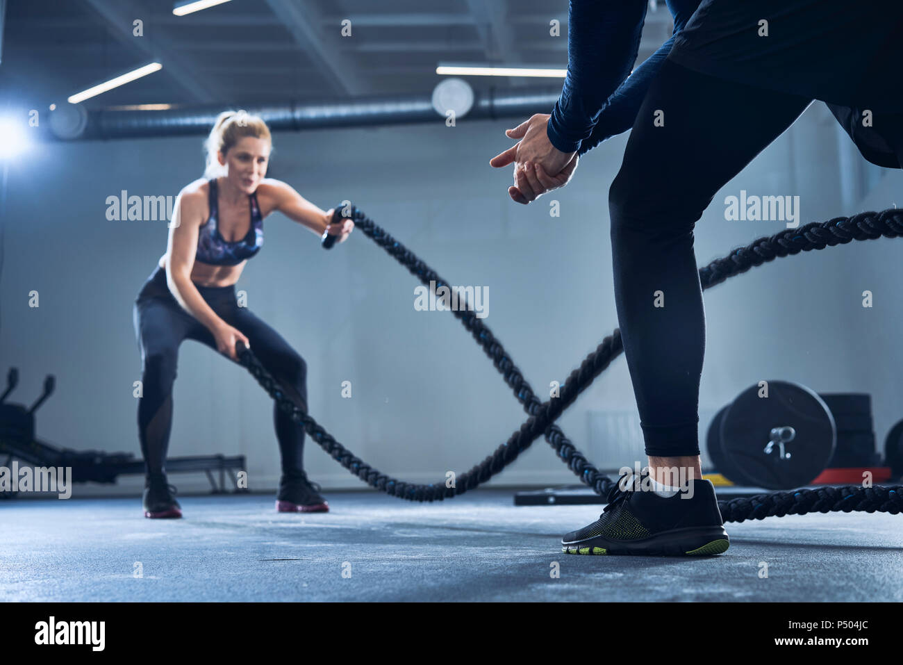 Mujer atlética battlerope haciendo ejercicio con un entrenador personal en un gimnasio Foto de stock