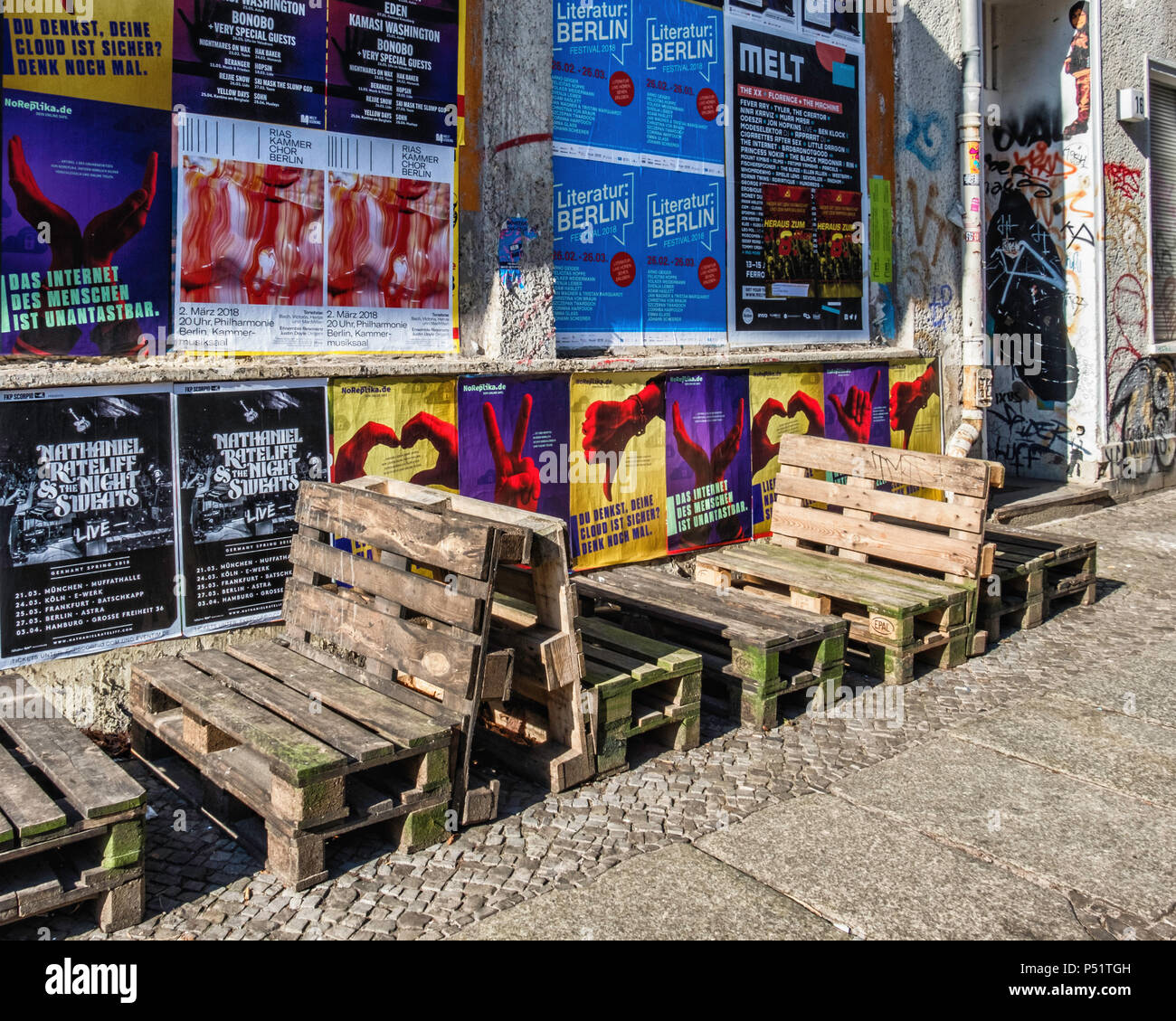 Kreutzigerstrasse, Friedrichshain, Berlín. Vista de la calle con mesas y sillas hechas de materiales reciclados paletas de madera y paredes cubiertas de carteles y pintadas Foto de stock