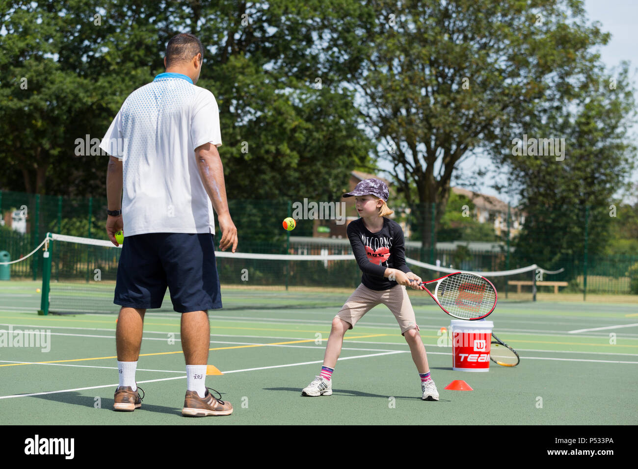 Sesión de entrenamiento de tenis para niños / lección teniendo lugar sobre una pista de tenis de tamaño completo con niños / Niños y Entrenador de tenis profesional, en verano. En el Reino Unido. (99) Foto de stock