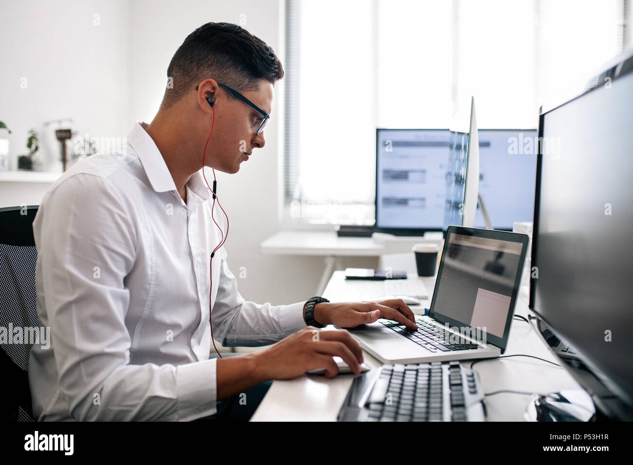 Desarrollador de software estaba sentado en su escritorio de oficina trabajando en el portátil usando auriculares. Llevar gafas hombre trabajando en un PC en la oficina. Foto de stock