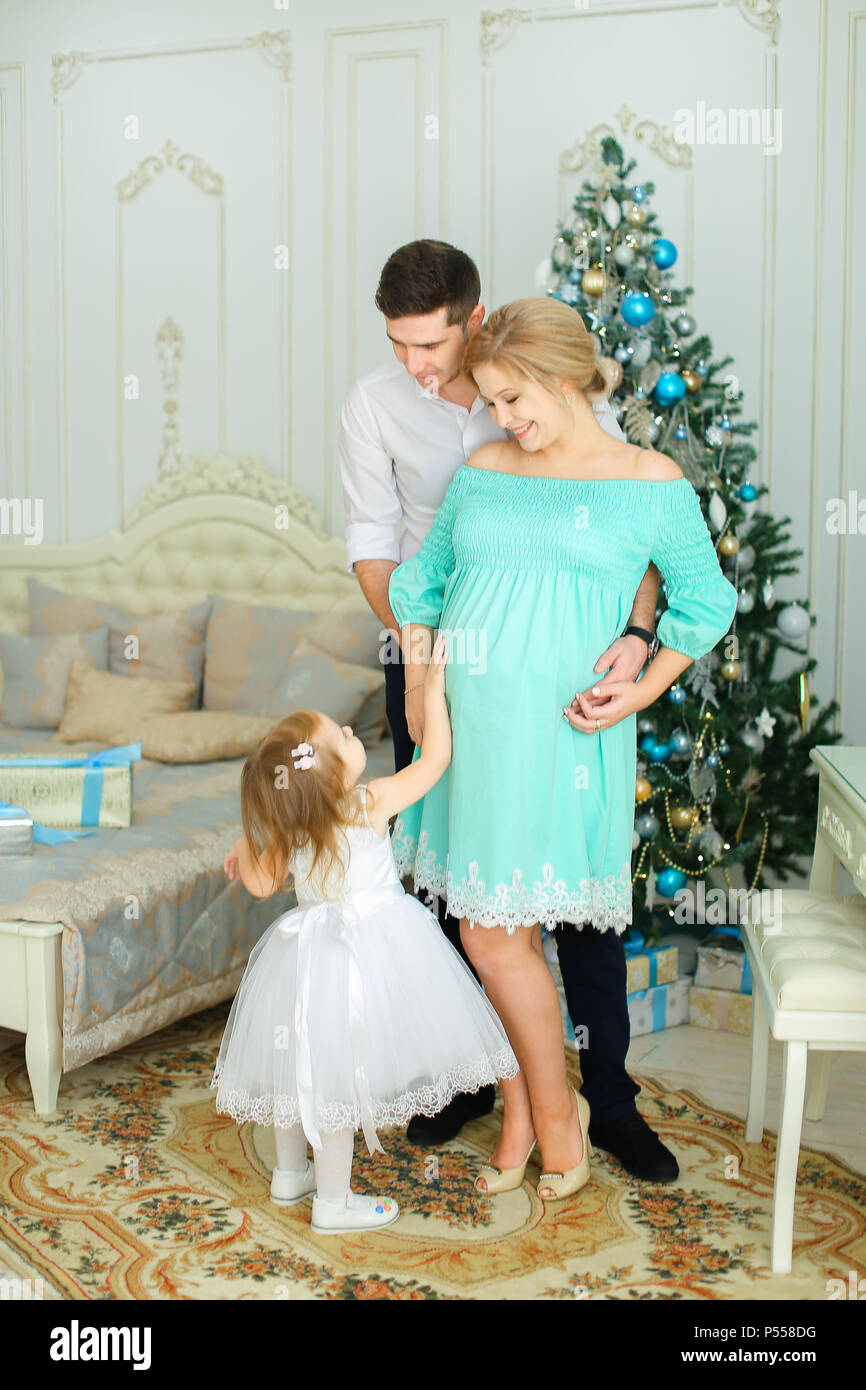 Mujeres embarazadas persona vistiendo vestido azul de pie con esposo e pequeña cerca del árbol de Navidad Fotografía de - Alamy