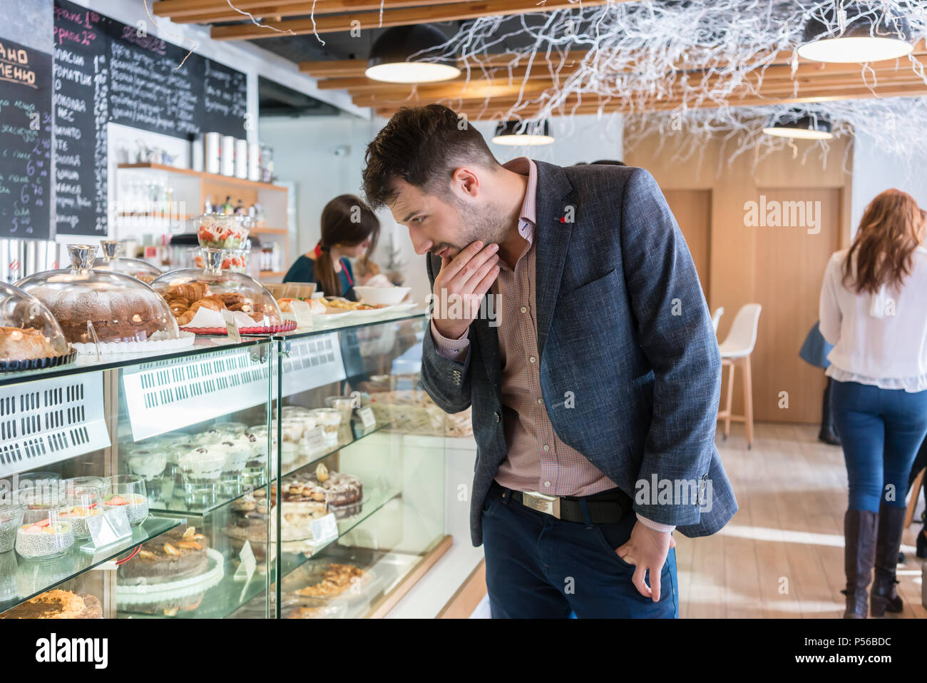 Hombre mirando indecisos diversos pasteles expuestos en el escaparate Foto de stock