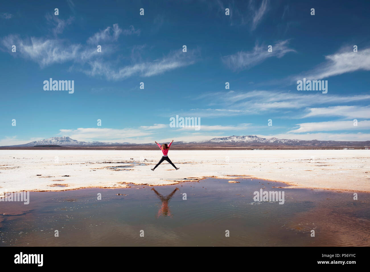 Feliz saltando al lado de un charco natural de sal en el Salar de Uyuni, Bolivia. Foto de stock