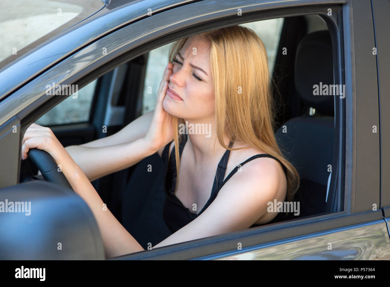 Mujer rubia tener dolor de muelas, mientras que la conducción de automóviles Foto de stock