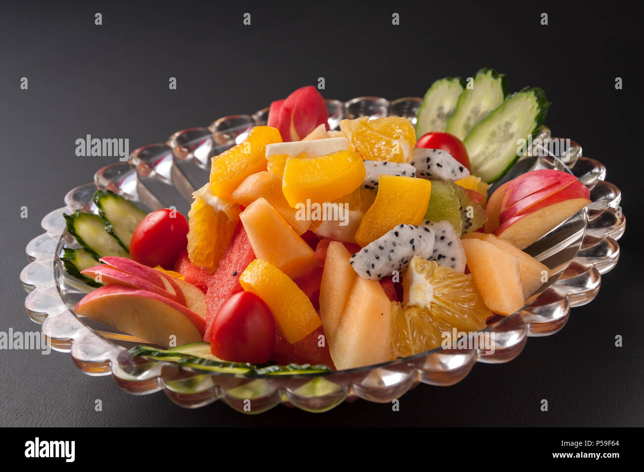 Colorido plato de frutas con sandía, melón, uvas, naranjas, fruta del dragón y menta Foto de stock