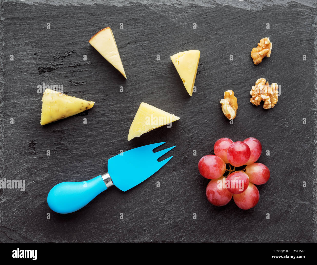 Tabla de quesos distintos quesos con uvas y nuez sobre placa de pizarra negra.vista superior Foto de stock