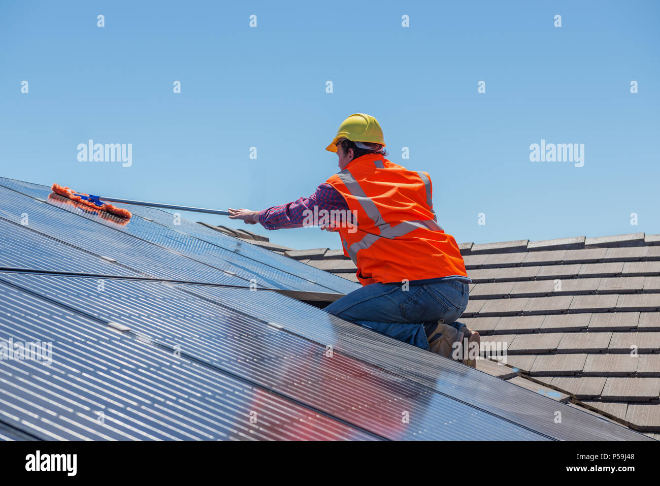 Joven trabajador limpieza de paneles solares en el techo.Se centra en el trabajador. Foto de stock