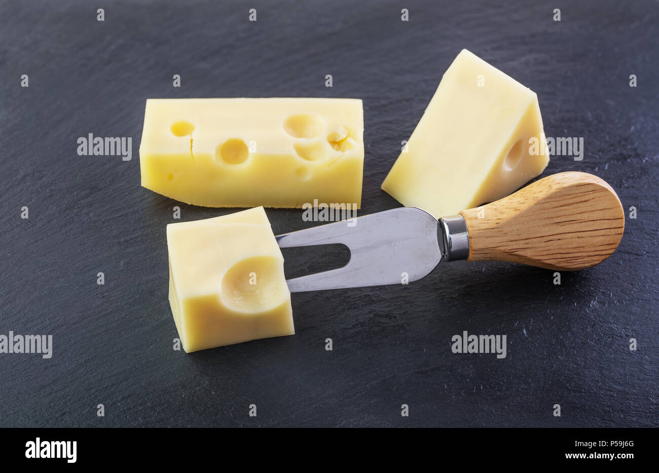 Tres trozos de queso sobre una placa de pizarra de piedra negra Foto de stock