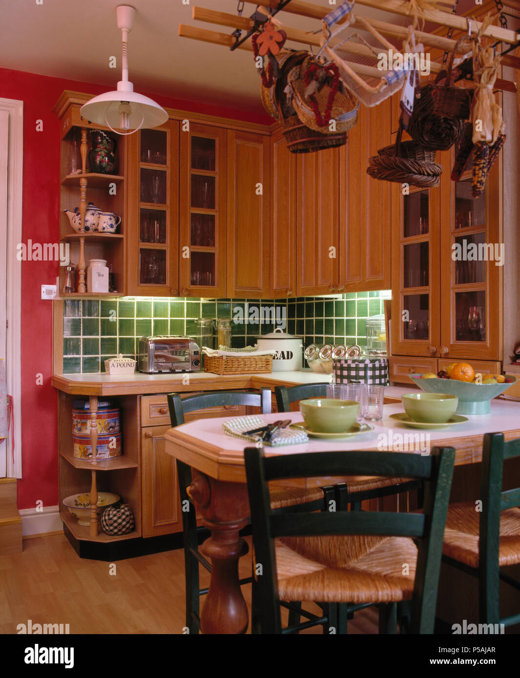 Rush verde sentado a la mesa, sillas para comer en la cocina del país rosa con azulejos verdes por encima de la encimera Foto de stock