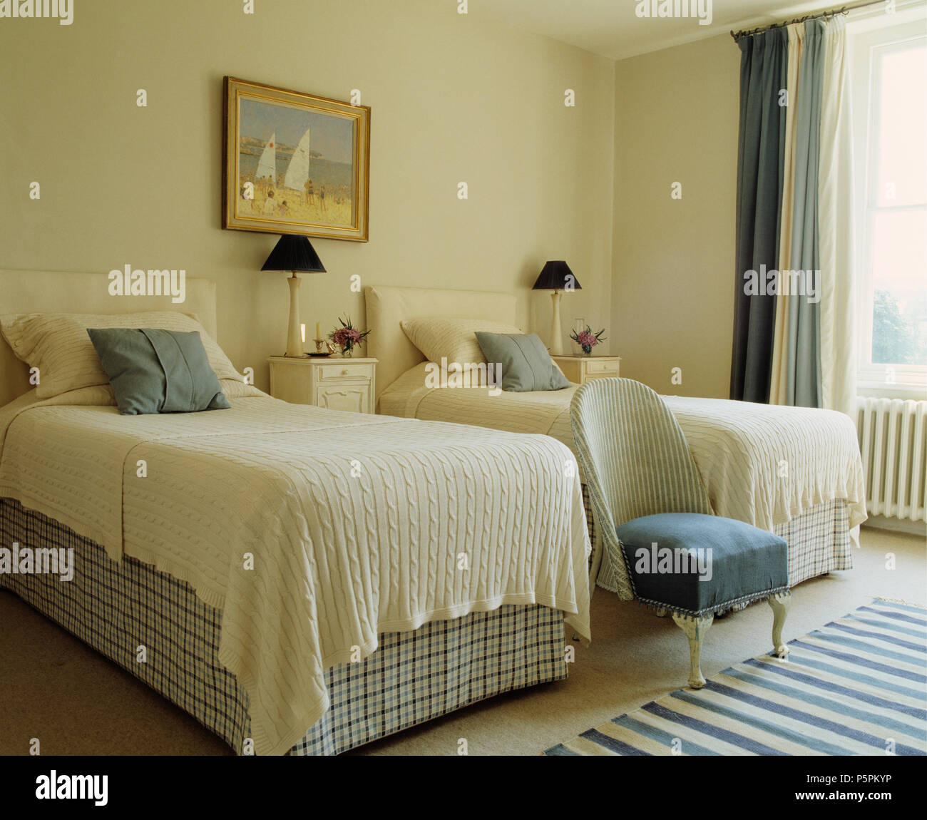 Mantas de lana crema sobre camas con marcada vallances en dormitorio con una crema vintage Lloyd Loom silla Foto de stock