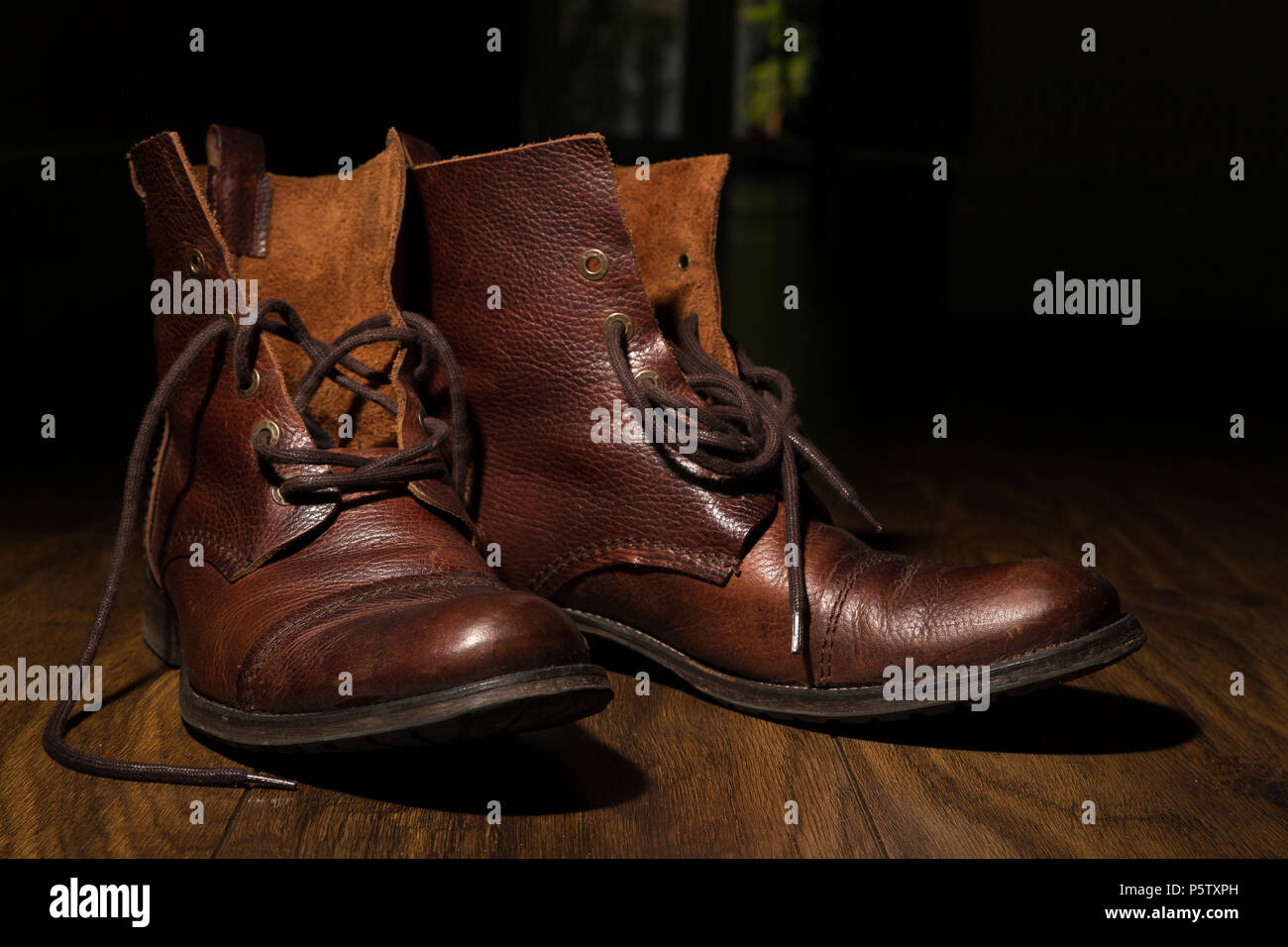 Primeros planos de botas de piel tradicionales, marrones para hombre, sin  cordones, en suelo laminado de madera dentro de un pasillo oscuro.  Iluminación artística de teclas bajas Fotografía de stock - Alamy