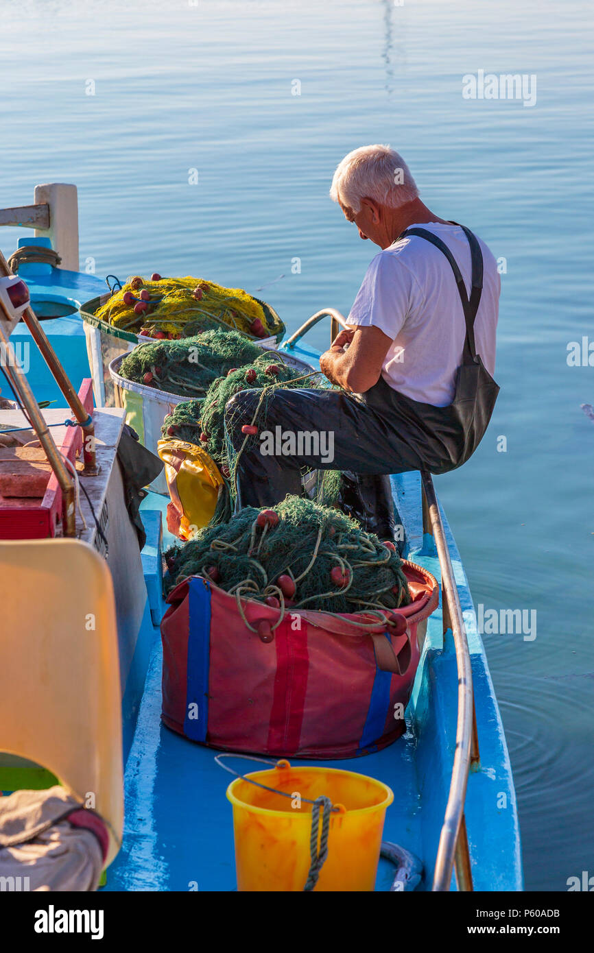 Los pescadores locales la reparación de las redes de pesca en un tradicional barco de pesca amarrados en el puerto antiguo, en Ayia Napa, Chipre Foto de stock
