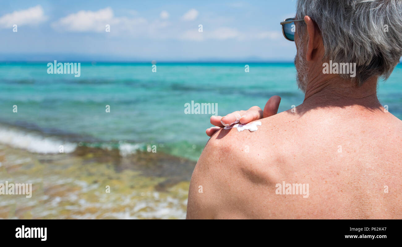 Hombre Senior aplicar loción de sol en vacaciones de verano vista posterior Foto de stock