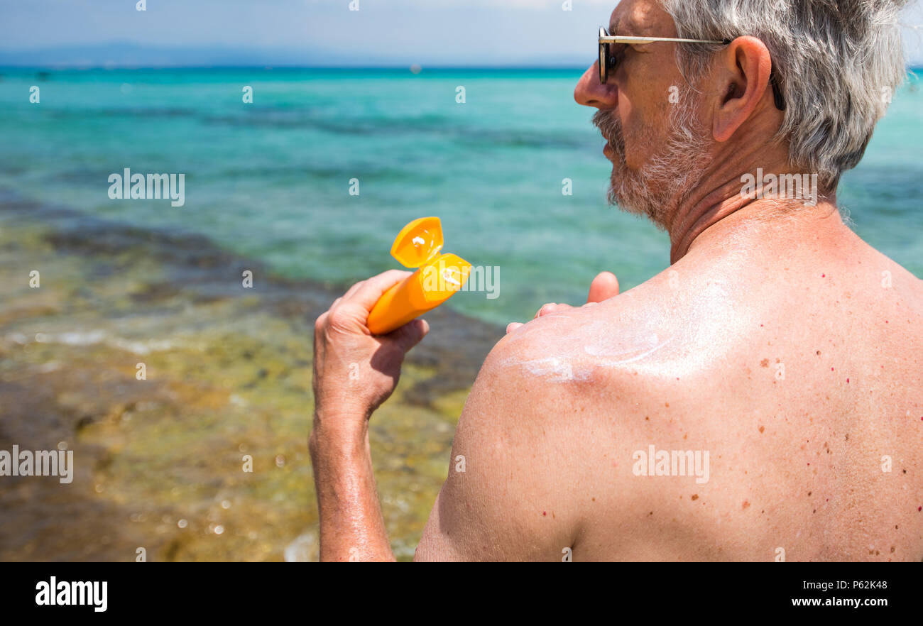 Hombre Senior aplicar loción de sol en vacaciones de verano vista posterior Foto de stock