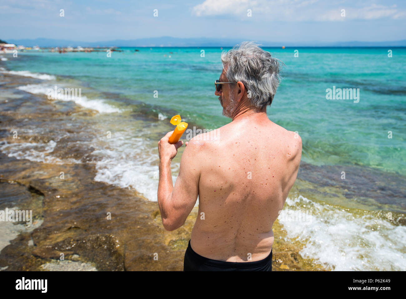 Hombre Senior aplicar loción de sol en vacaciones de verano vista posterior Foto de stock